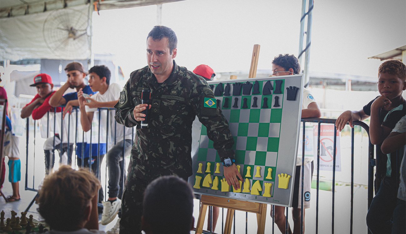 O sargento Nathaniel, vice-campeão de xadrez no Norte, explica as técnicas do esporte aos alunos. O quadro magnético e peças fazem parte do material doado pelo projeto Fotos: Rotary Club Boa Vista Caçari
